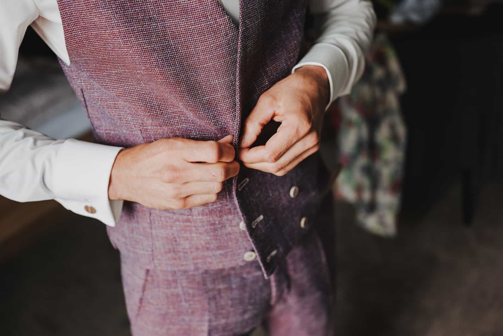 Detailaufnahme eines Bräutigams, der seine Weste vor der standesamtlichen Hochzeit in Lohberg zuknöpft, fotografiert vom Hochzeitsfotografen Niklas Hesser.