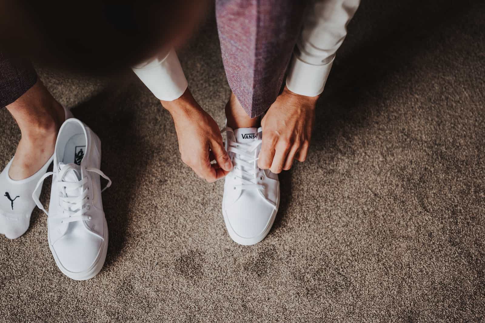 Detailaufnahme eines Bräutigams, der seine weißen Vans-Sneaker für die standesamtliche Hochzeit in Lohberg schnürt.