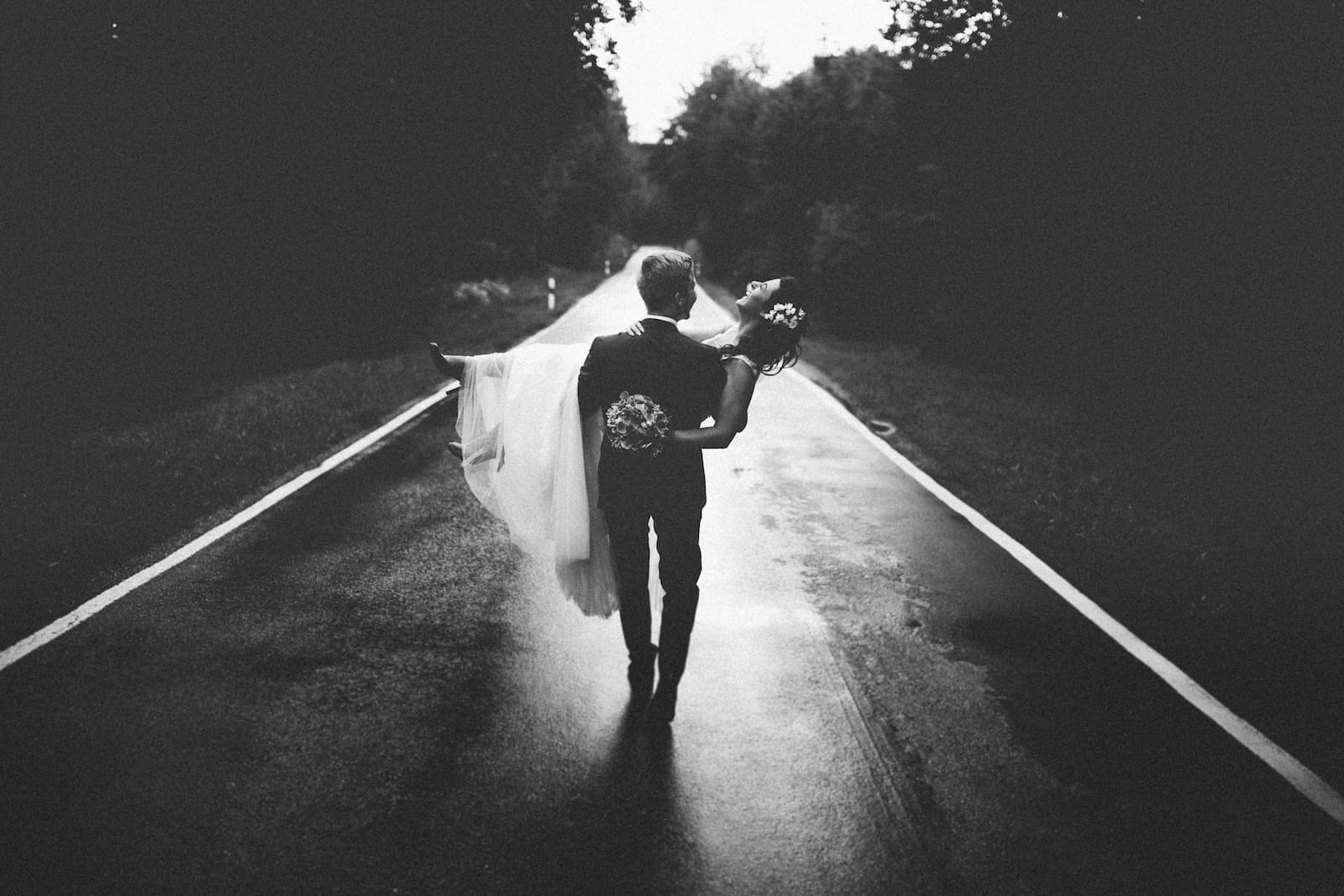 Hochzeitsfotografie in Wüstenrot: Ein Bräutigam trägt seine Braut auf einer Landstraße, eingefangen vom Hochzeitsfotografen Niklas Hesser.