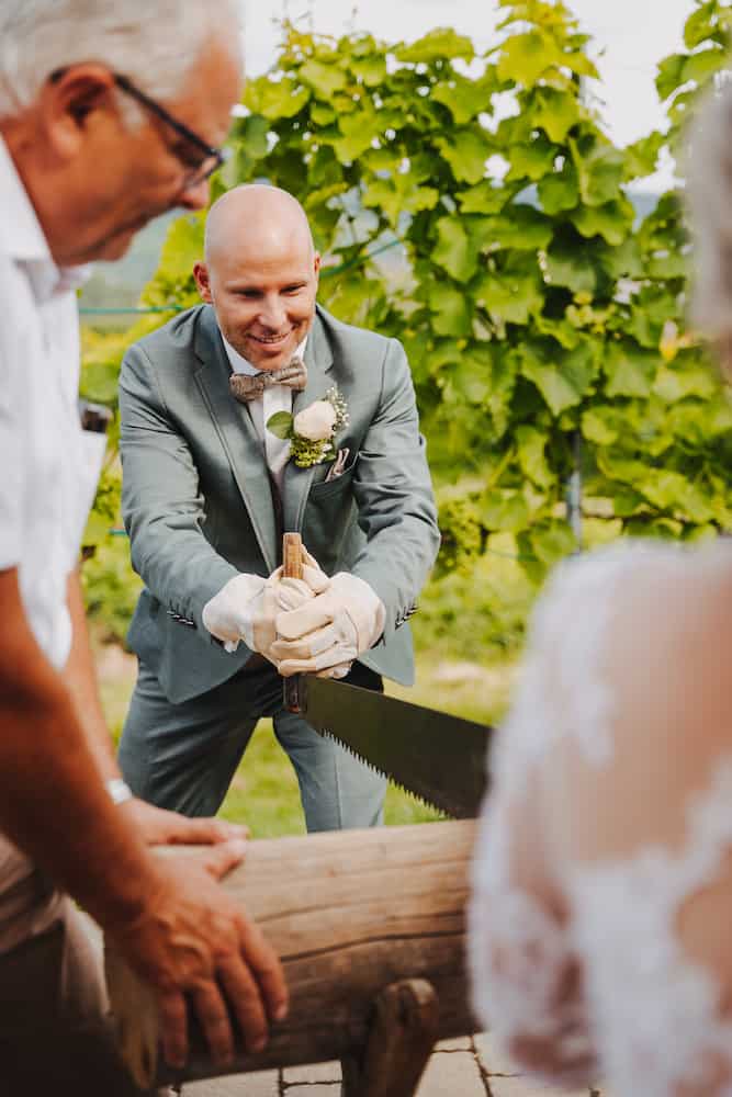 Hochzeitsfotografie in Kernen: Bräutigam beim traditionellen Baumstammsägen, festgehalten vom Hochzeitsfotografen Niklas Hesser.