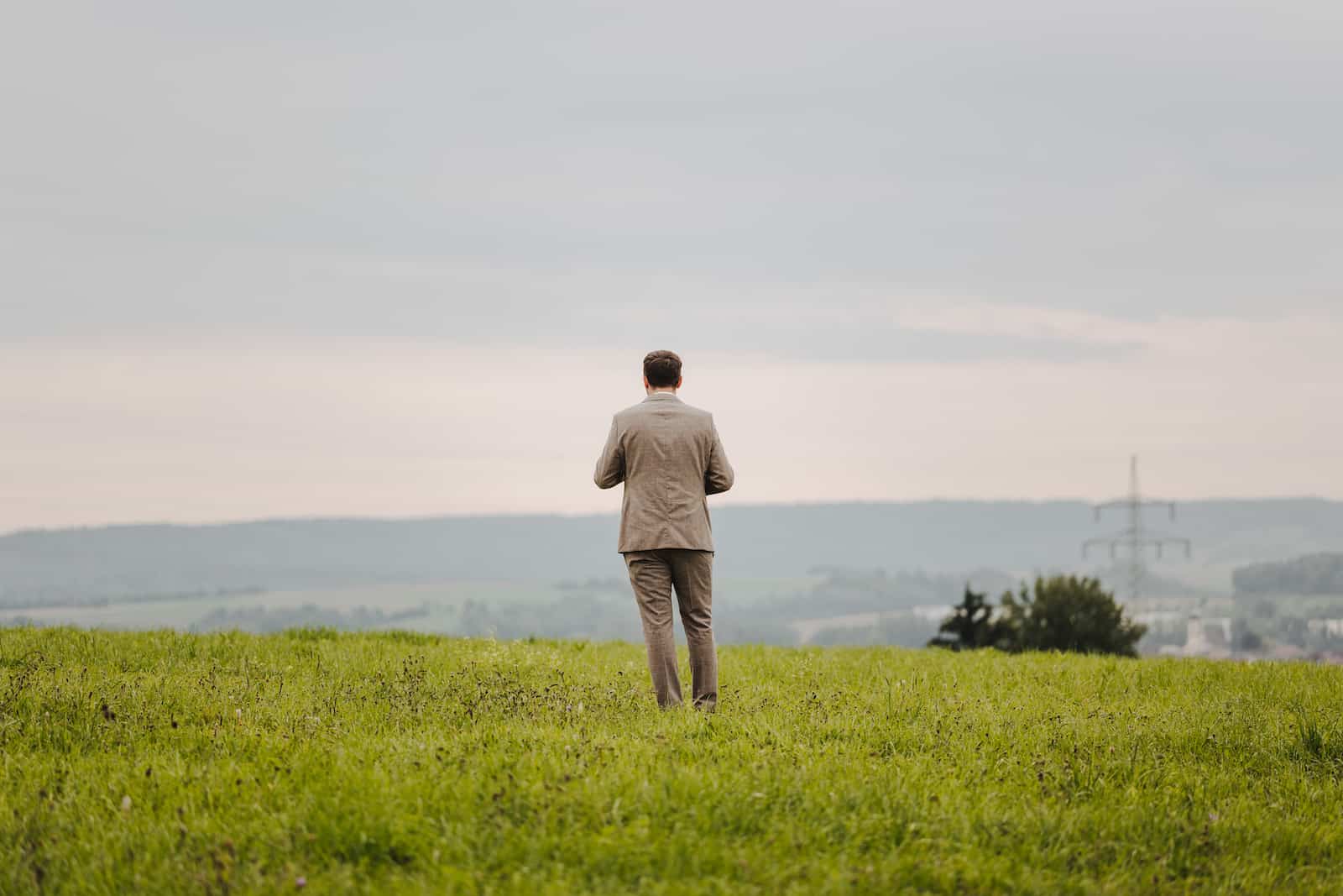 Hochzeitsreportage in Langenbeutingen: Ein Bräutigam in einem Anzug steht auf einer grünen Wiese und blickt in die Ferne. Hochzeitsfotograf Heilbronn.