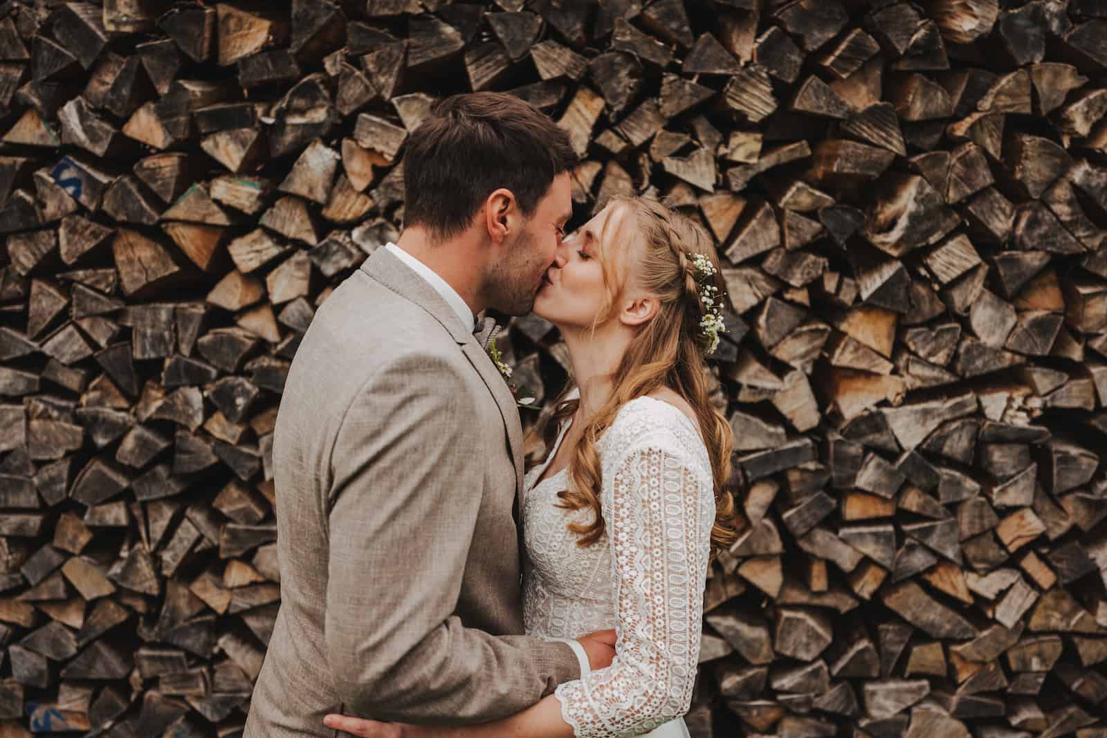 Hochzeitsreportage in Langenbeutingen: Ein Brautpaar küsst sich vor einem rustikalen Holzstapel, fotografiert vom Hochzeitsfotografen Niklas Hesser.