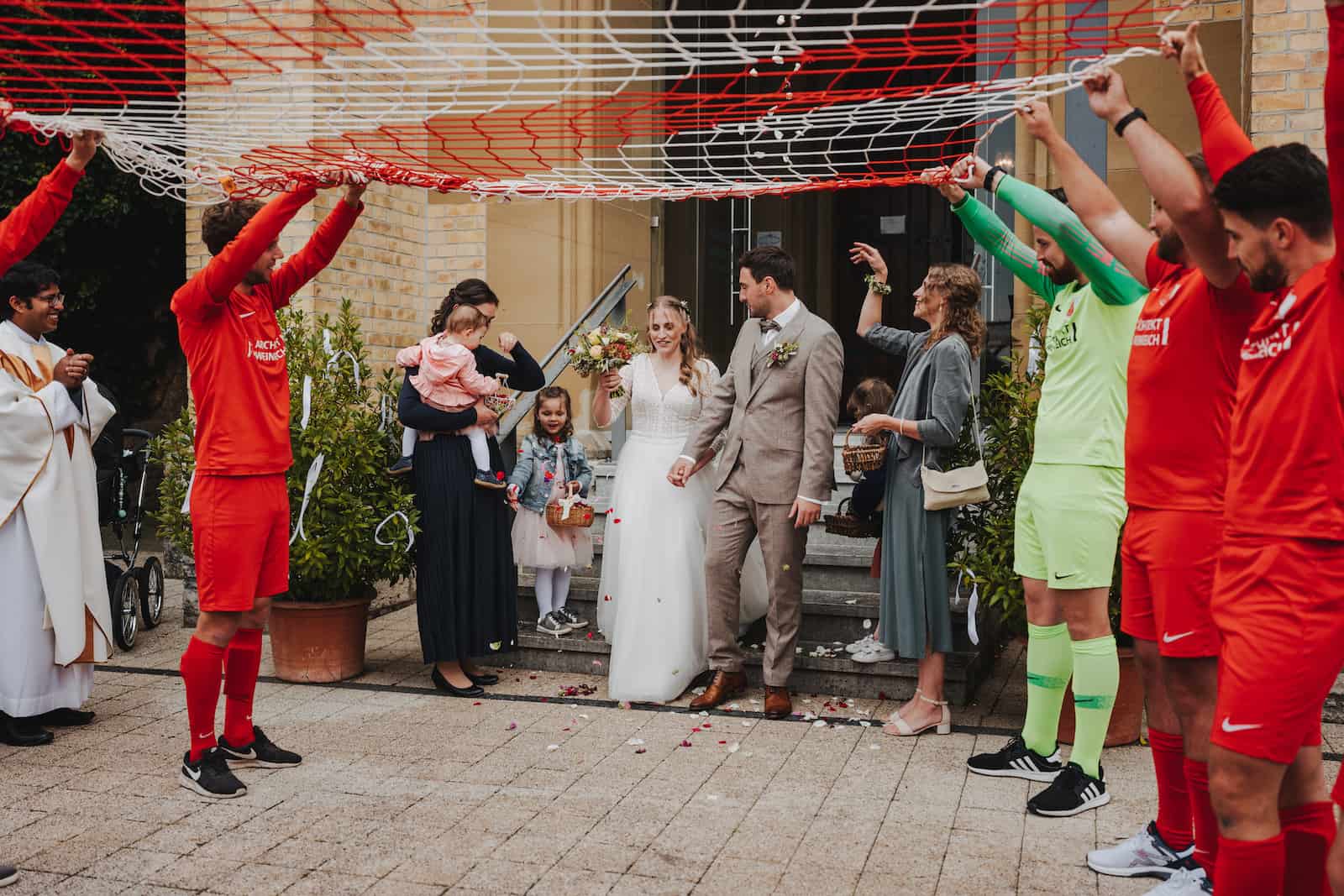 Hochzeitsreportage in Langenbeutingen mit einem Brautpaar, das unter einem Fußballnetz hindurchgeht, fotografiert vom Hochzeitsfotografen Niklas Hesser.