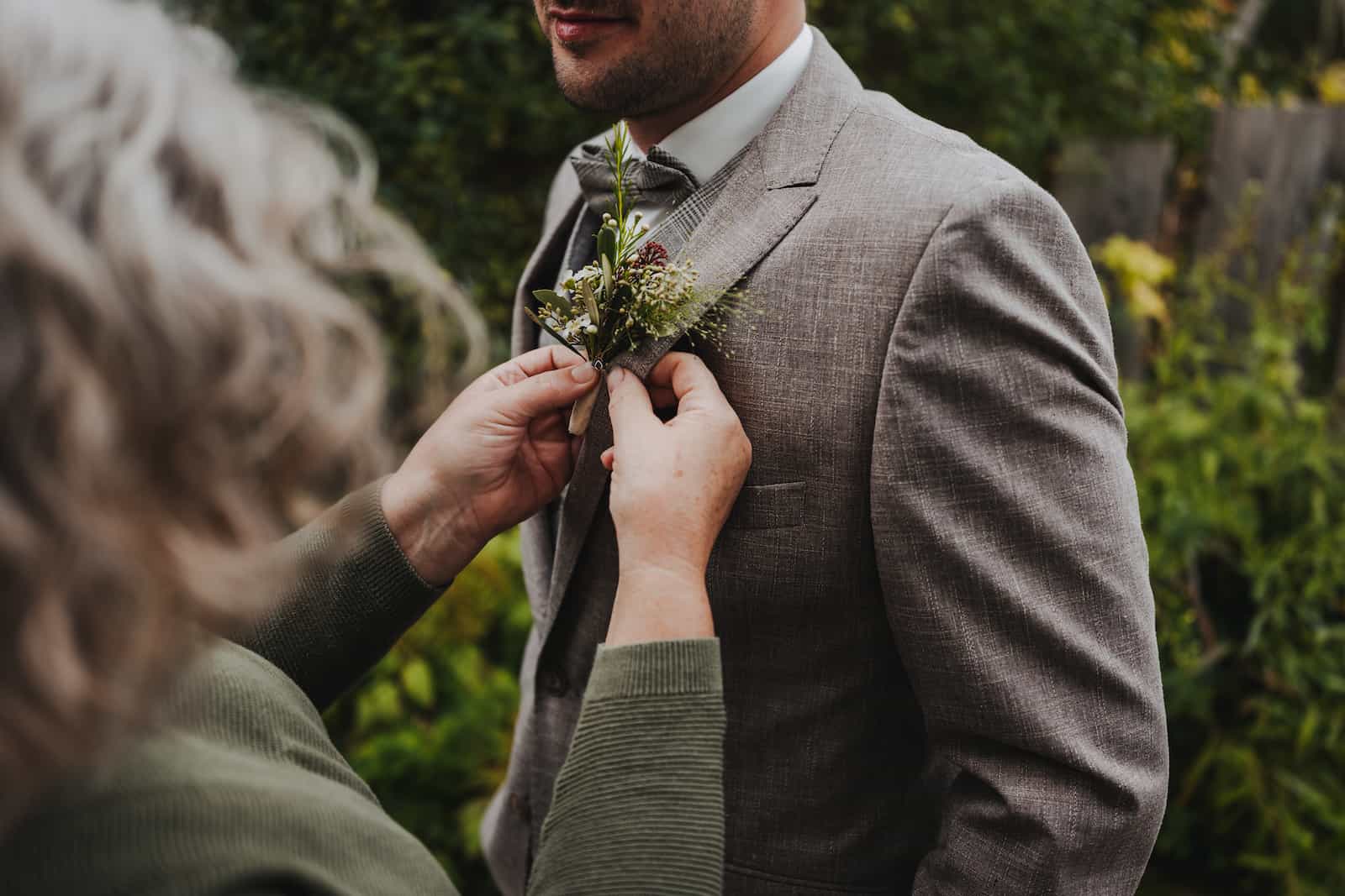 Detailaufnahme eines Bräutigams, der eine Blume am Revers befestigt bekommt, aufgenommen bei einer Hochzeitsreportage in Langenbeutingen vom Hochzeitsfotografen Niklas Hesser.