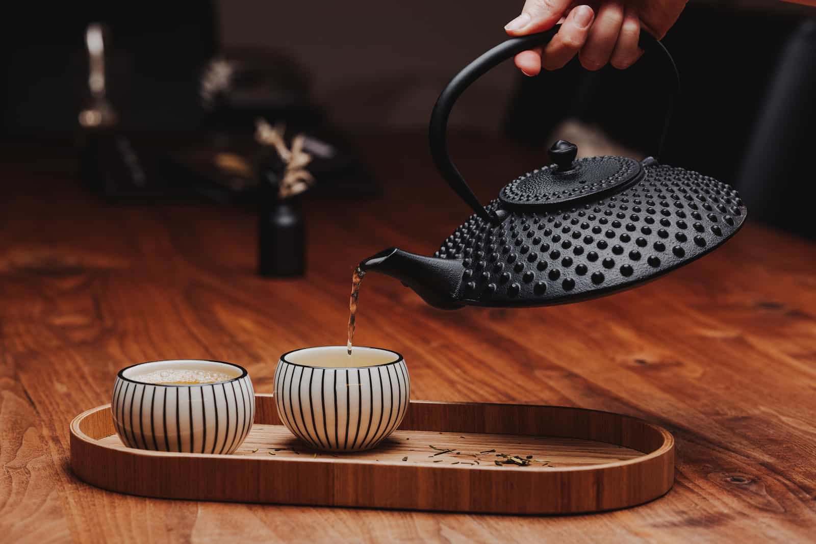 Detailaufnahme einer Teekanne, die Tee in zwei Tassen auf einem Holztisch gießt, fotografiert vom Eventfotografen Niklas Hesser in Heilbronn.