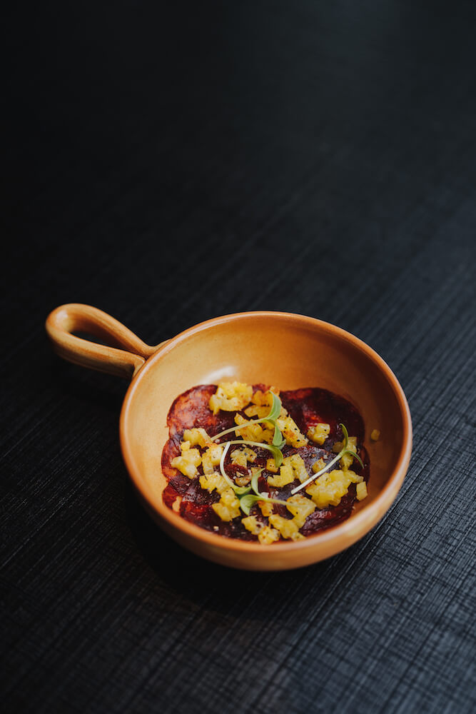 Food-Fotografie eines stilvoll angerichteten Gerichts in einer braunen Schale auf dunklem Hintergrund.