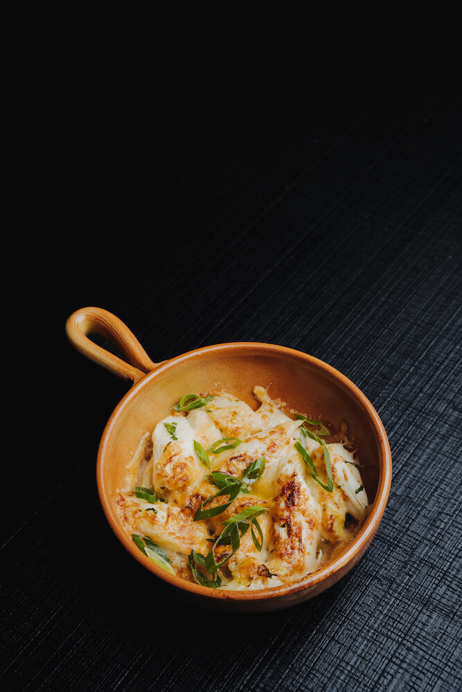 Food-Fotografie eines gratinierten Gerichts in einer braunen Schale auf dunklem Hintergrund.