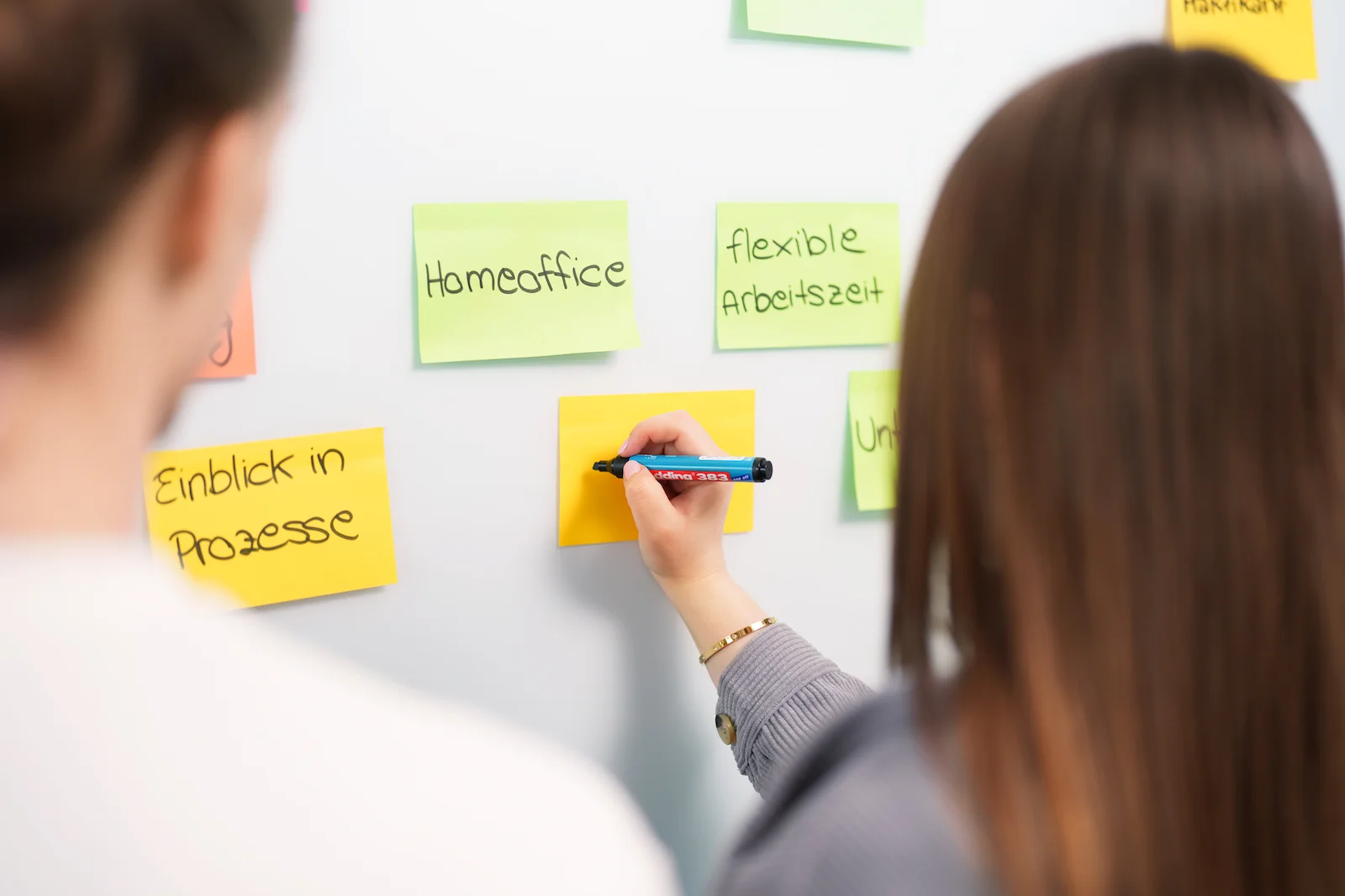 Businessfotografie in Heilbronn: Mitarbeiter schreiben Notizen auf bunte Haftnotizen an einer Wand.
