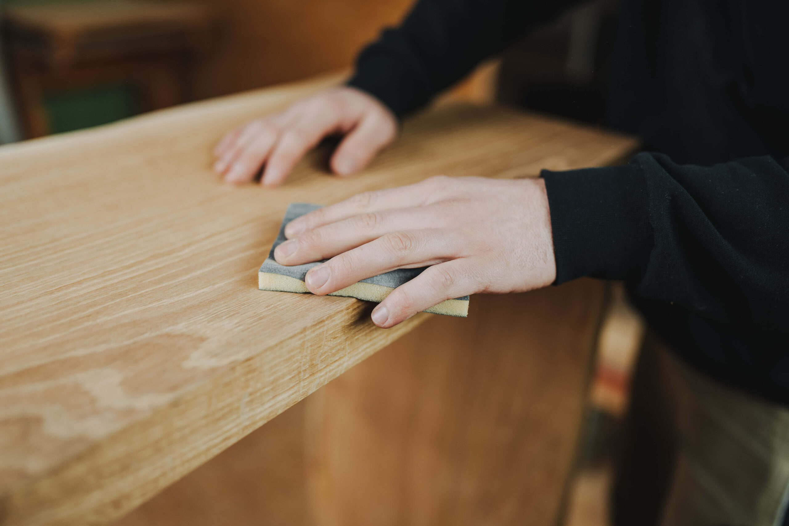 Detailaufnahme eines Corporate-Shootings in Obersulm, das die Hände einer Person beim Schleifen eines Holztisches zeigt.