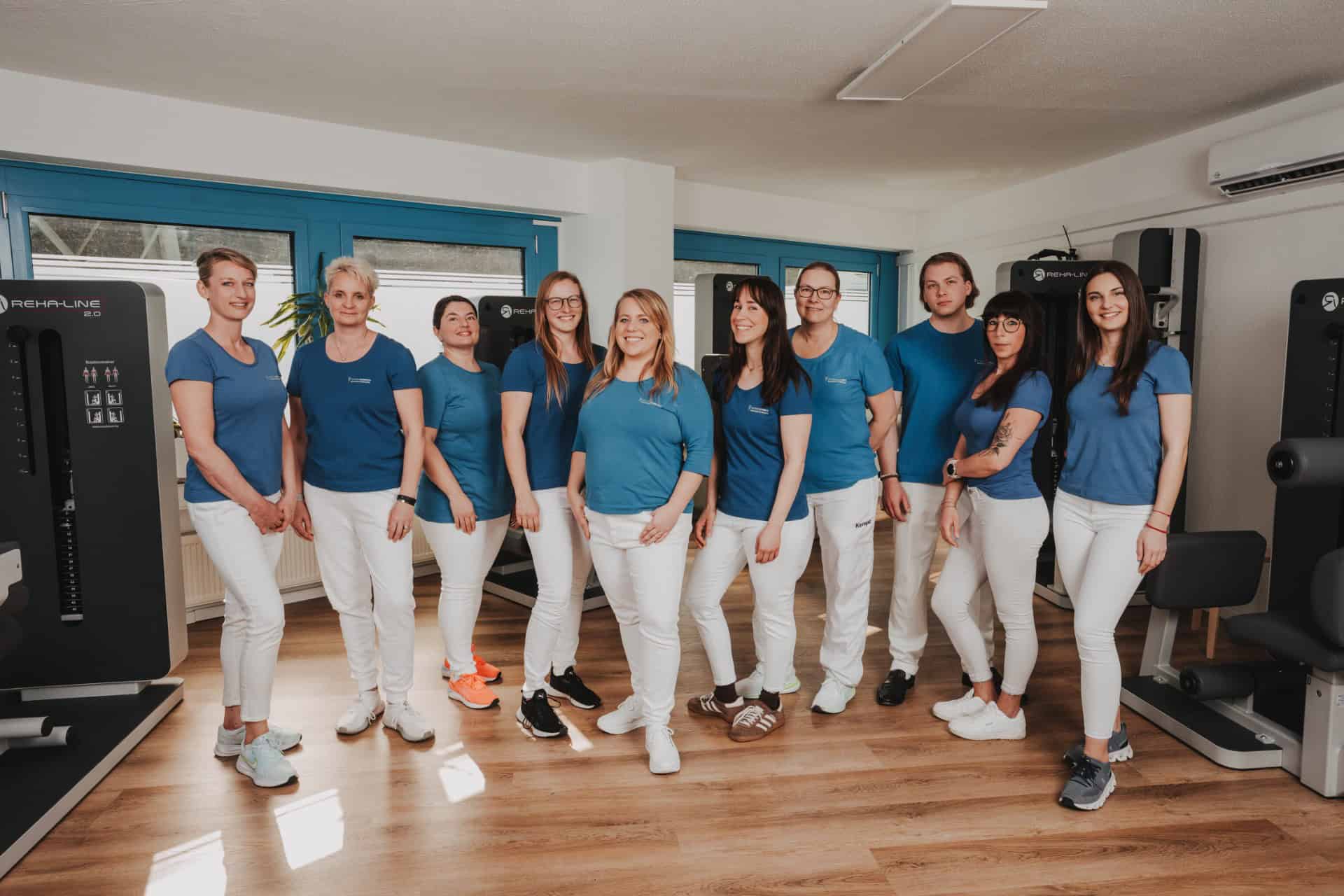 Das gesamte Team von PhysioLogisch Erlenbach in blauen Shirts beim Teamfoto im modernen Geräteraum mit REHA-LINE 2.0 Trainingsgeräten
