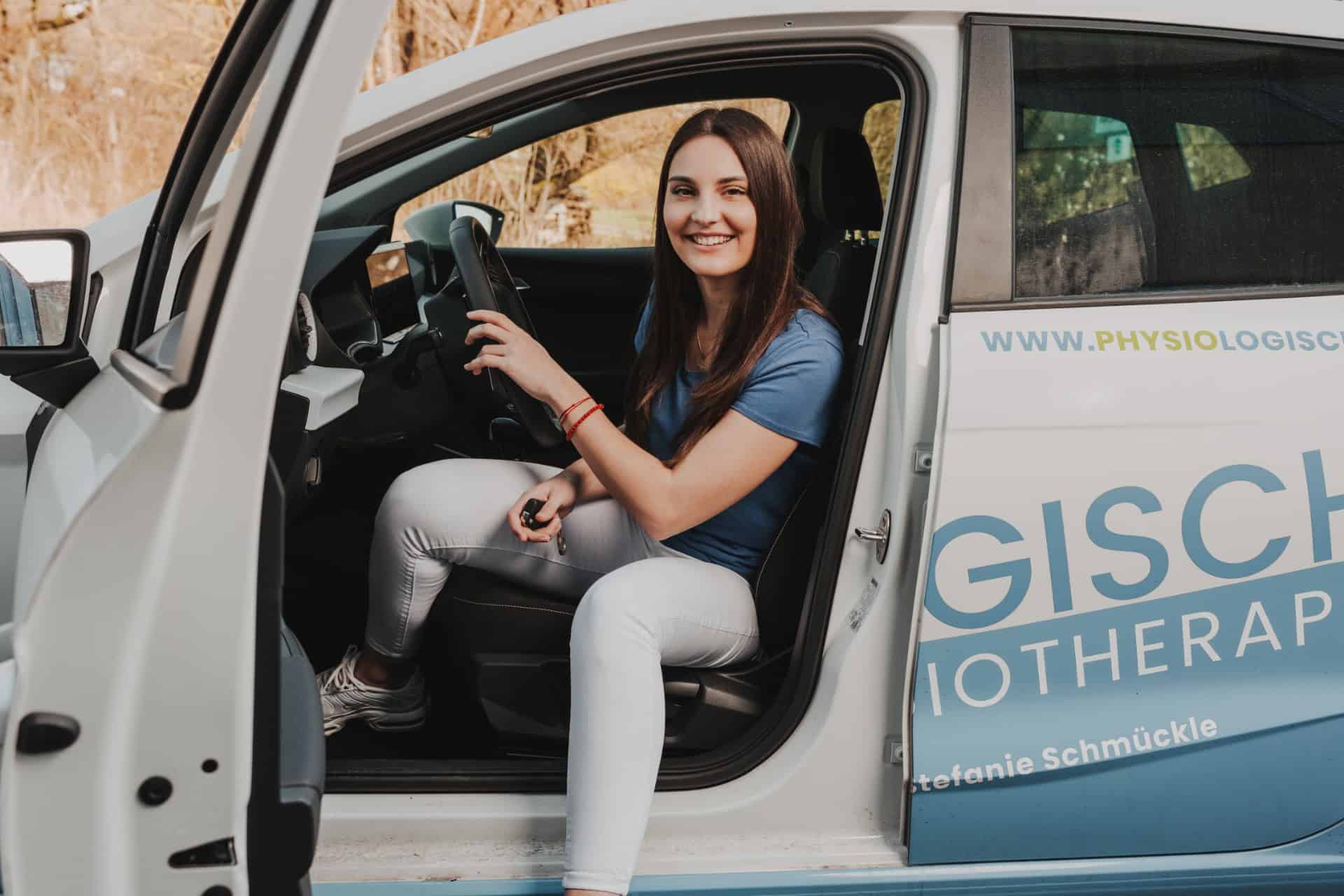 Physiotherapeutin von PhysioLogisch Erlenbach sitzt lächelnd im Praxisfahrzeug für Hausbesuche, mit sichtbarem Logo auf der Fahrzeugtür
