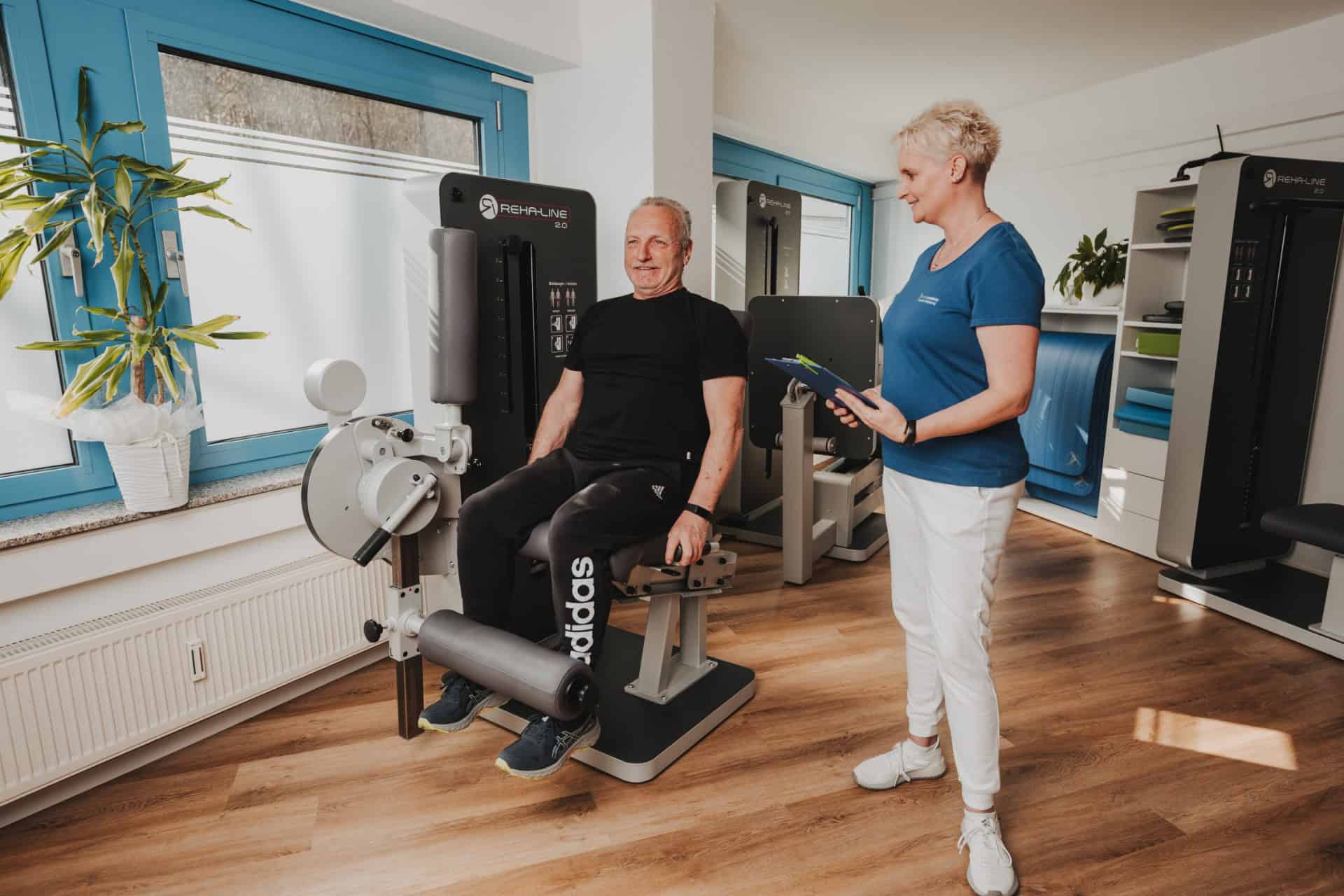 Blick in den hellen Praxisraum von PhysioLogisch Erlenbach mit REHA-LINE Trainingsgeräten, Therapeutin betreut Patienten beim Reha-Training