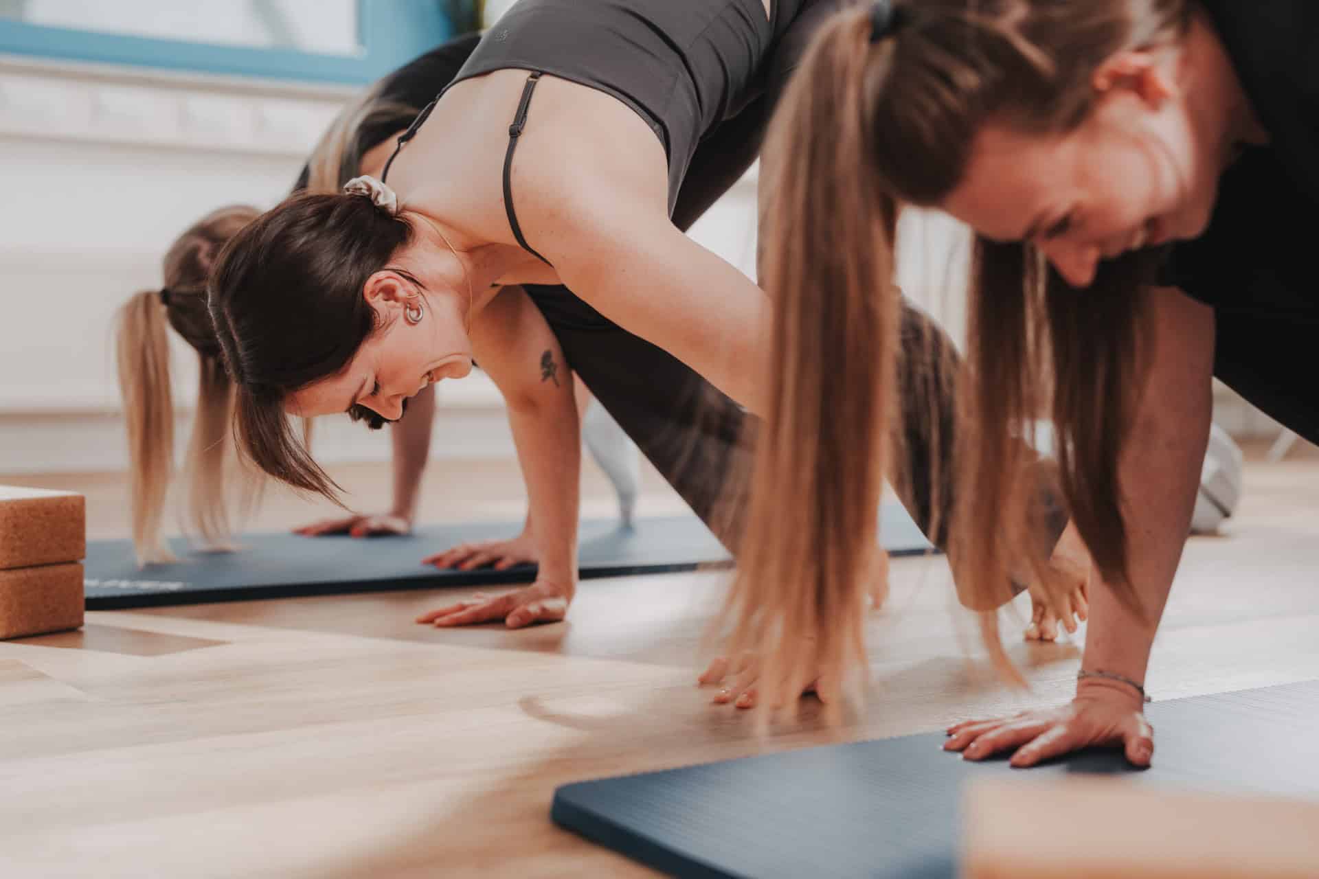 Yoga-Gruppe bei PhysioLogisch Erlenbach in dynamischer Downward-Dog-Übung auf blauen Matten, Yoga-Blöcke im Vordergrund