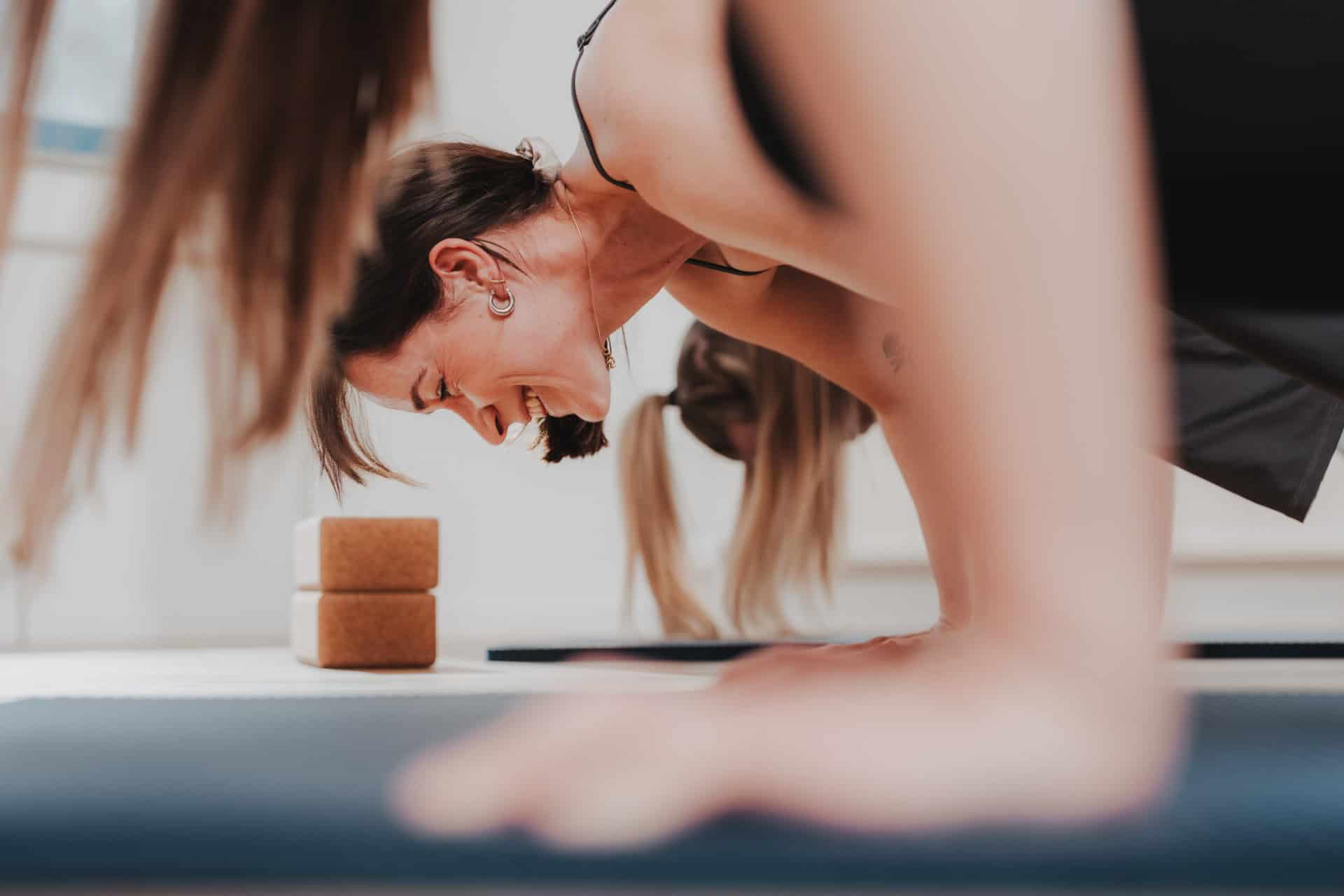 Lachende Frau beim Yoga-Kurs von PhysioLogisch Erlenbach in Downward-Dog-Position, Kork-Yoga-Blöcke im Vordergrund